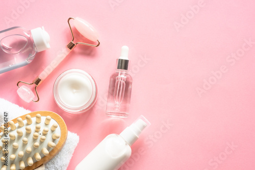 Natural cosmetics on pink. Skin care product, cream, soap serum, jade roller and white towel. Flat lay image with copy space.