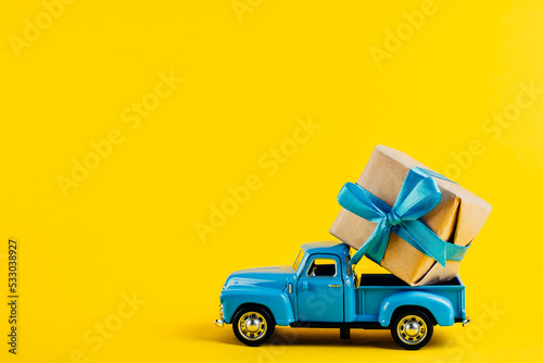 Toy blue car with a gift on a bright yellow background