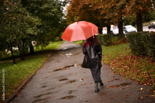 a brown-haired woman with a red umbrella walks through the quiet streets of an autumn city