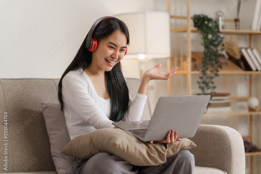 Young happy asian woman using laptop and headphones online meeting with friends via online conference remote meeting. Young happy asian woman using laptop and headphones online meeting with friends via online conference remote meeting.