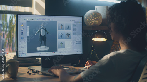 Male young 3D designer having remote work on 3D modeling and designing clothes using pc with professional software while sitting at the table at home
