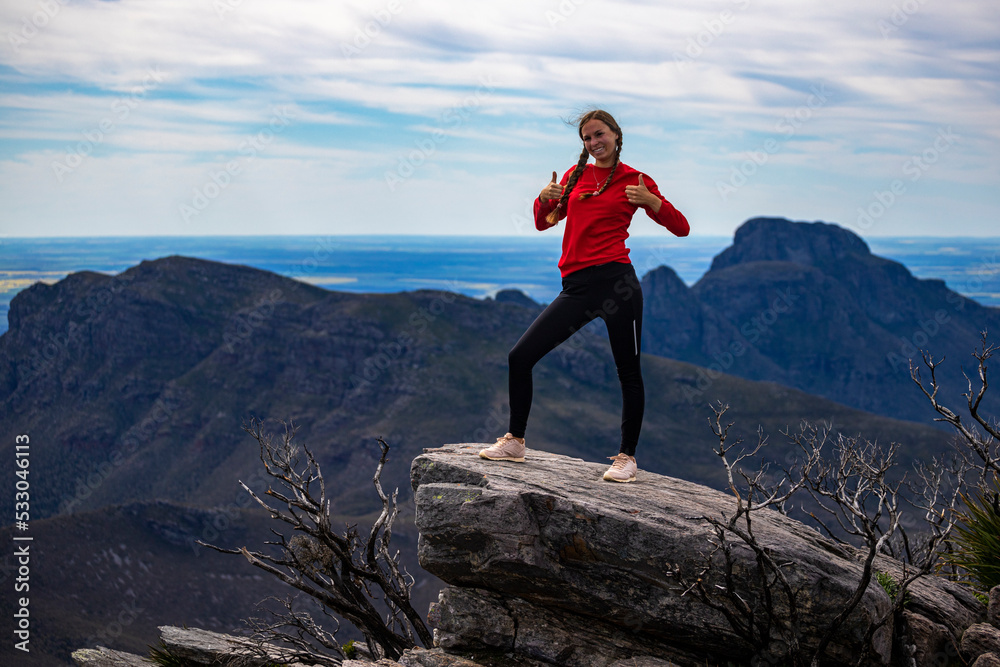 girl with pigtails on top of a mountain overlooking a green mountain range in the background; bluff knoll, highest peak in western australia