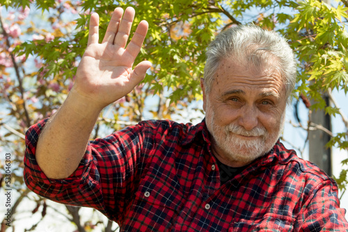 Elderly gentleman is waving with his hand to say hello 