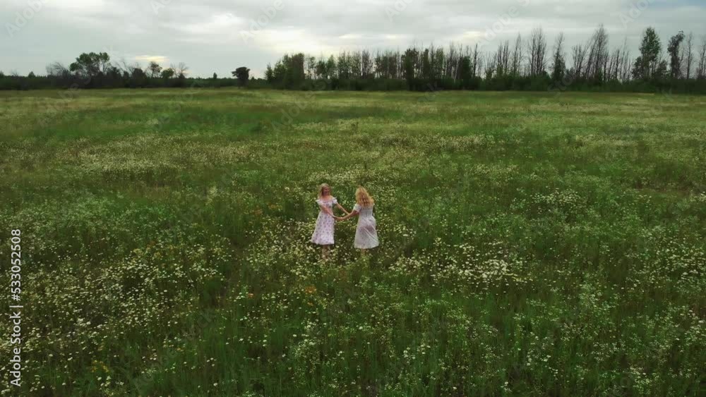 Two young women in light summer dresses holding hands on the field Two young women in light summer dresses holding hands on the field