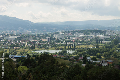 Panoramic top view of Kislovodsk with houses among green cypresses and other plants and the horizon in a hazy haze on a sunny summer day and a space for copying