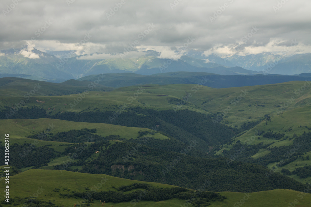 Panoramic view of green mountains and hills from the Bermamyt plateau in Karachay-Cherkessia in Russia on a cloudy summer day and a copy space