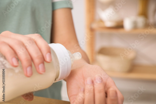 Woman checking temperature of infant formula indoors, closeup with space for text. Baby milk