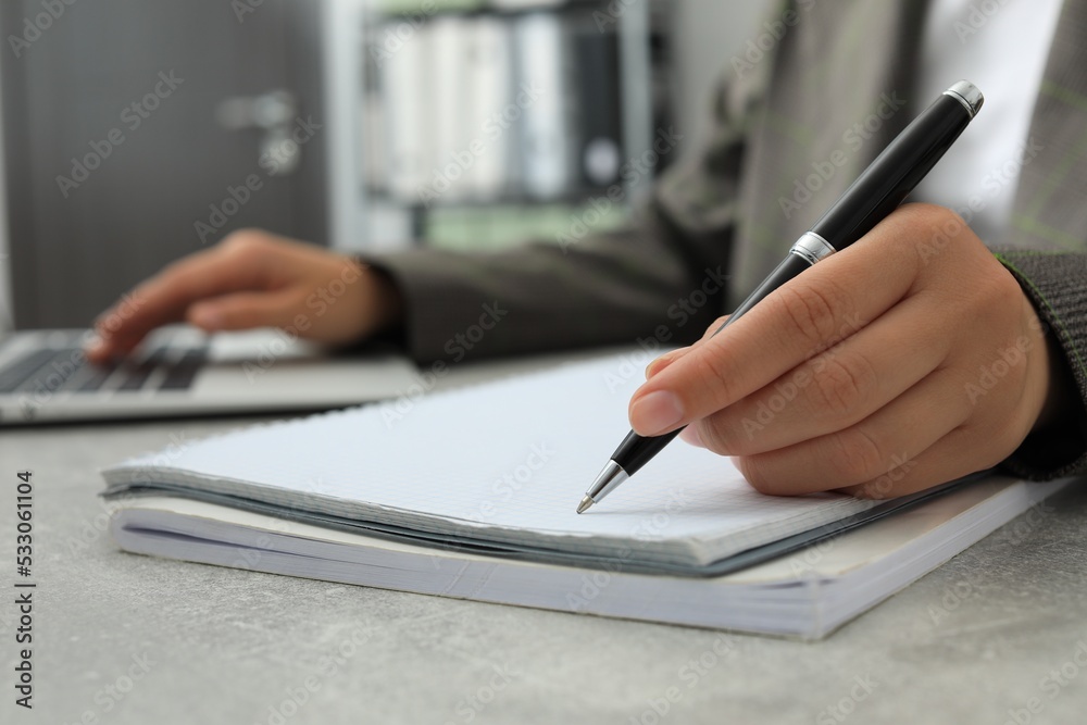 Woman working with laptop and writing in notebook at table indoors, closeup Woman working with laptop and writing in notebook at table indoors, closeup