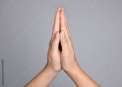 Woman holding hands clasped while praying against light grey background, closeup