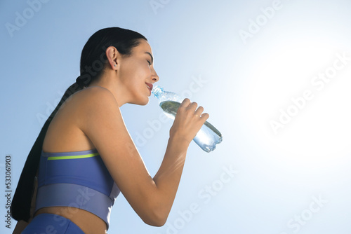Beautiful young sportswoman drinking water outdoors. Refreshing drink