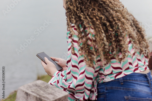 Latin woman with curly hair and cell phone in hand typing photo