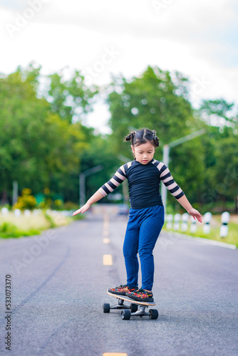 Child or kid girl playing surfskate or skateboard in skating rink or sports park at parking