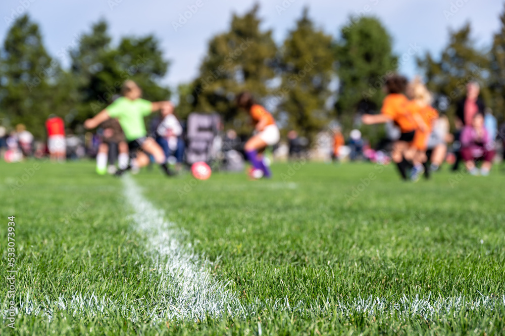 Selective focus on ground level view of soccer field center line with defocused youth girls in background Selective focus on ground level view of soccer field center line with defocused youth girls in background
