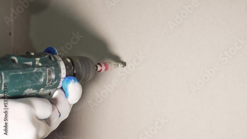 The builder screws the drywall with screws using a cordless screwdriver to the wall in close-up.