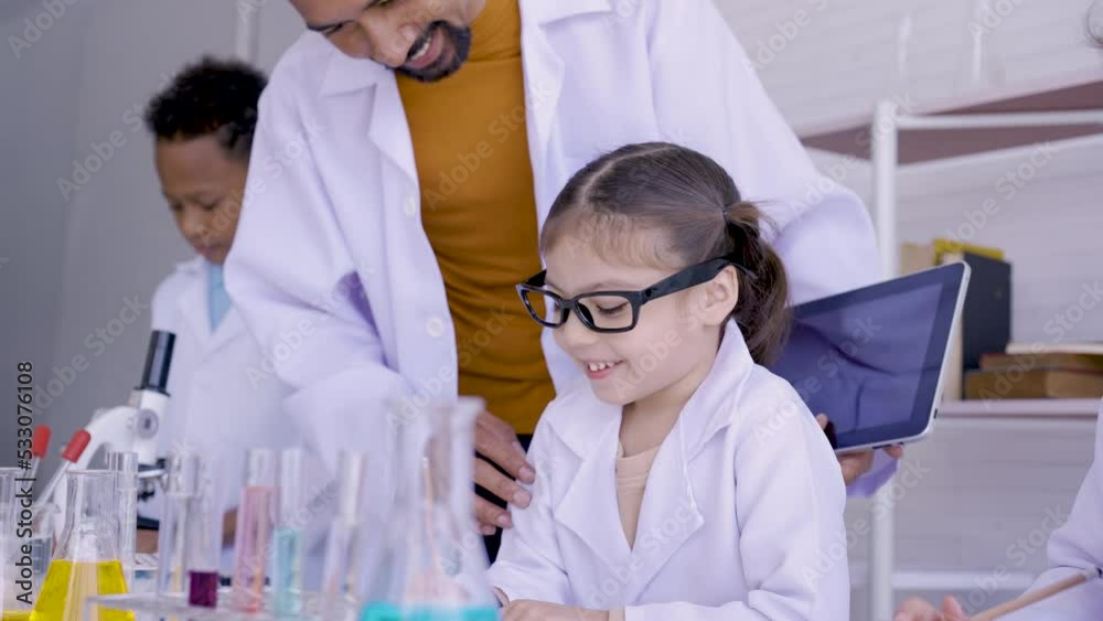 4K, In a science classroom, little girl is interested in writing down what teacher is teaching. Bearded male teacher introducing science to students in class. Concept education, Science experiments 4K, In a science classroom, little girl is interested in writing down what teacher is teaching. Bearded male teacher introducing science to students in class. Concept education, Science experiments