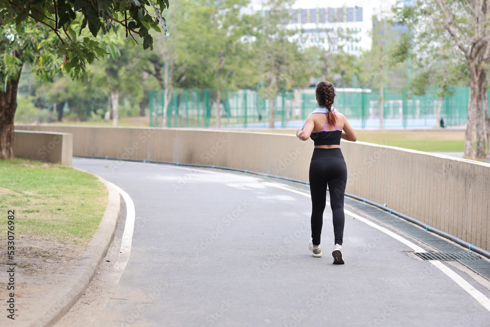 Portrait of sporty young asian woman in sportswear jogging outdoor for marathon training. Jogger girl exercising along concrete path outdoor with green tree background. Sport concept