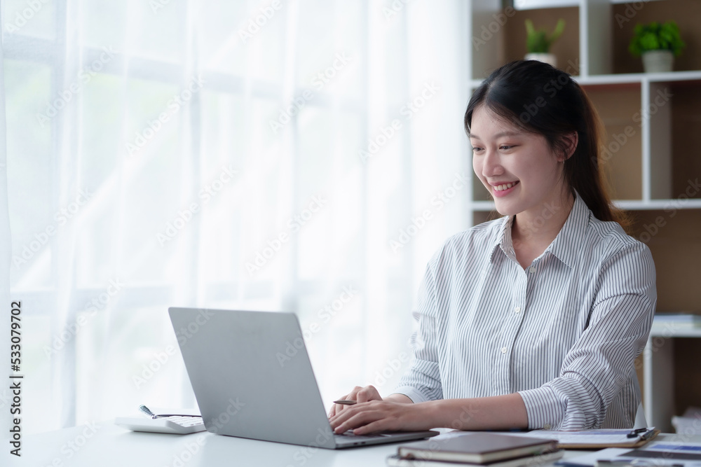 Bright and charming young Asian woman working on her laptop with the intention of producing a satisfying result. Bright and charming young Asian woman working on her laptop with the intention of producing a satisfying result.