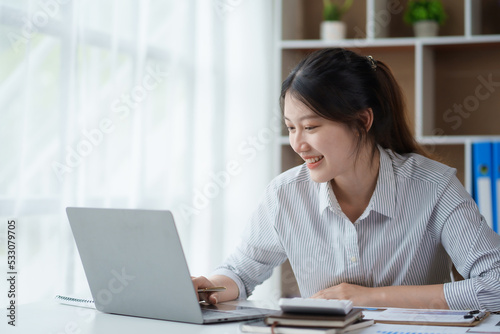 Bright and charming young Asian woman working on her laptop with the intention of producing a satisfying result.