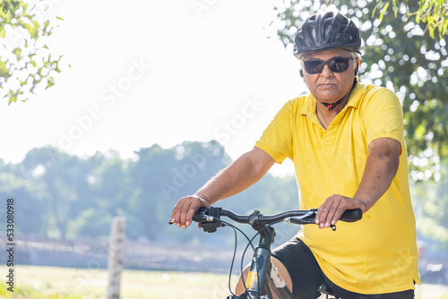 Thoughtful senior man in protective sportswear leaning on bicycle handlebar outdoors 