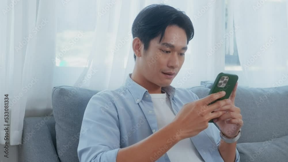Young asian man using  smart phone  on sofa in living room