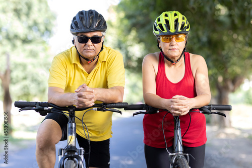 Fototapeta Naklejka Na Ścianę i Meble -  Confident senior couple cyclists leaning on handlebar of bicycle outdoors
