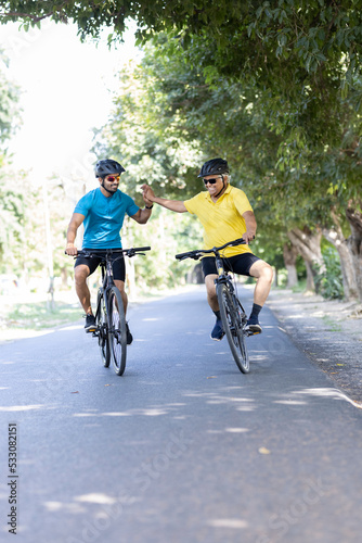Young man and old cyclist having fun riding bicycle outdoors on countryside road 
