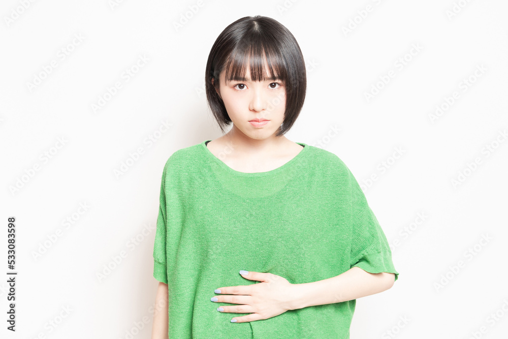 白背景の前で、お腹を手で抑える若い女性 白背景の前で、お腹を手で抑える若い女性