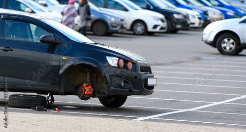 A car with a wheel removed is on a jack in a supermarket parking lot. Punctured wheel repair, service.