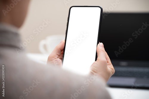 Cropped shot of businesswoman looking at blank screen smartphone in modern office room. woman hand holding phone with white screen in office. woman using cell phone at workplace