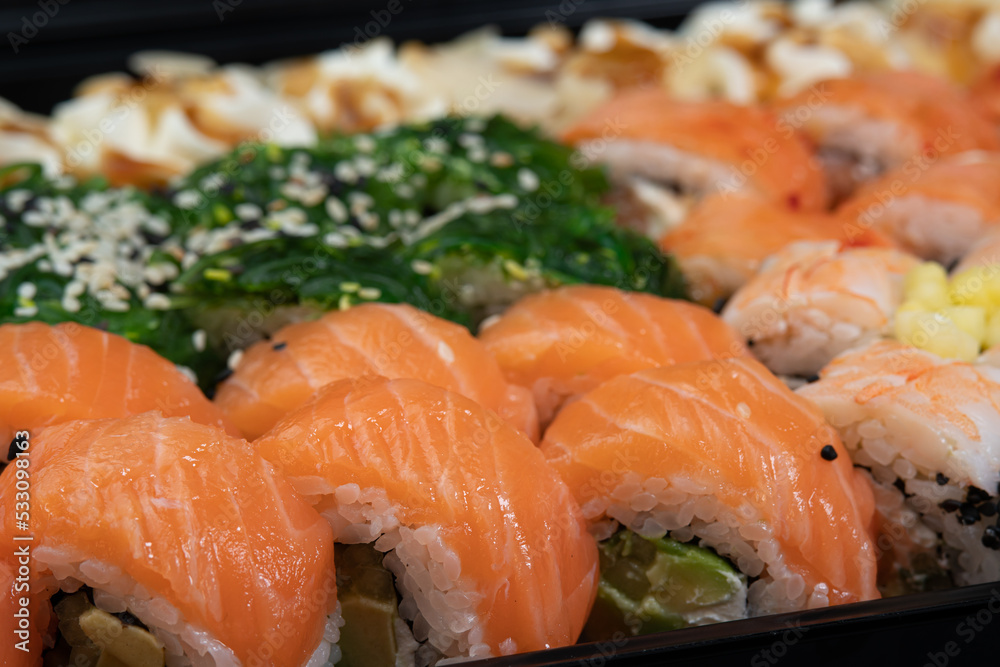 Sushi rolls background in package after delivery. Philadelphia roll in sushi set close up. Traditional Japanese food. Japanese kitchen with sea food. Taking one sushi roll from set using chopsticks Sushi rolls background in package after delivery. Philadelphia roll in sushi set close up. Traditional Japanese food. Japanese kitchen with sea food. Taking one sushi roll from set using chopsticks