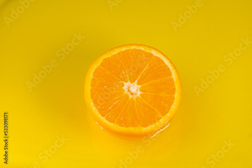 Water falling from orange hue orange on yellow background. Orange slice and water splashing, drops of juice falling from juicy fruit. Making cocktail of fruits, drinking cold lemonade