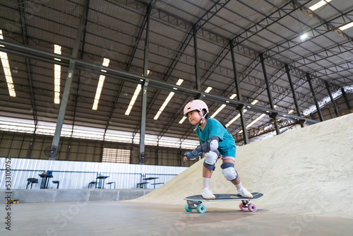 asian child or kid girl fun playing skateboard or ride surf skate and get off ramp or down from wave bank to bottom turn surfing in skatepark by extreme sports to wear helmet protect for body safety