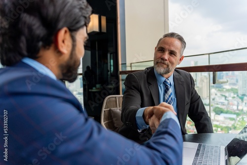 Portrait photo of a mature white caucasian businessman shaking hand with an asian businessman signaling they reach to an agreement deal for the contract that they are discussing about.