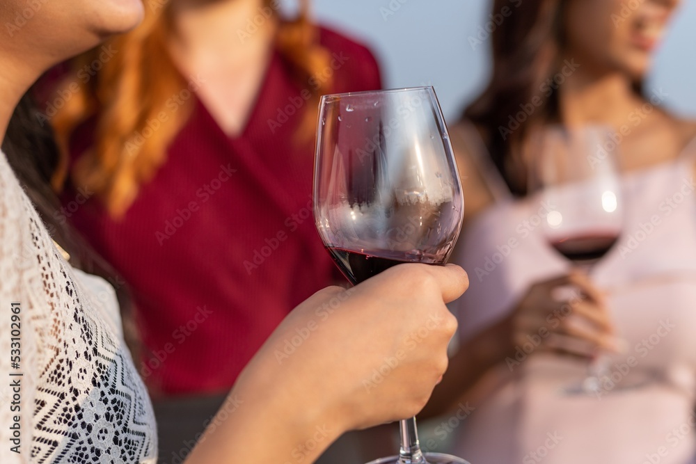 Photo of close up of the wineglass of a group of female friends cheering each other and enjoying their time in a rooftop bar in Bangkok during sunset time