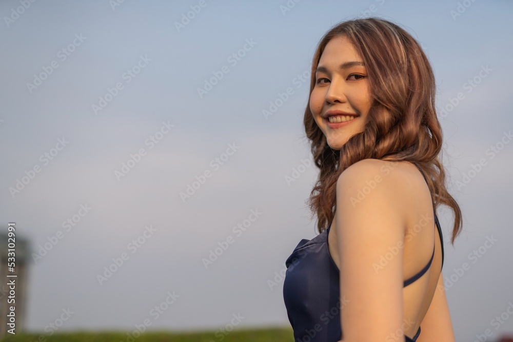 Photo of a young elegant sexy beautiful lady female model wearing nice blue dress at a rooftop bar in Bangkok, enjoying the sunset bath and view