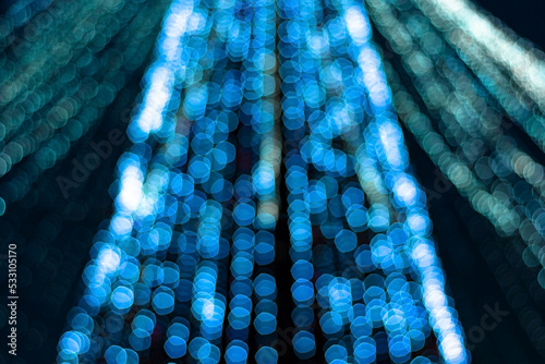 Festive blue xmas lights on christmas tree in urban central park at holiday evening in winter night, defocus shiny garland decoration glow in bright bokeh in dark downtown, blur image