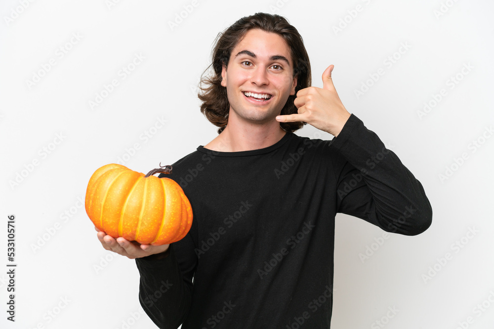 Young handsome man holding a pumpkin isolated on white background making phone gesture. Call me back sign Young handsome man holding a pumpkin isolated on white background making phone gesture. Call me back sign
