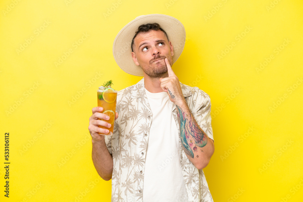 Young caucasian man holding a cocktail isolated on yellow background having doubts while looking up Young caucasian man holding a cocktail isolated on yellow background having doubts while looking up