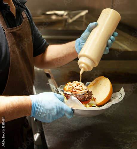man putting sauce on a hamburger
