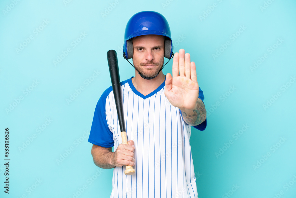 Baseball player with helmet and bat isolated on blue background making stop gesture