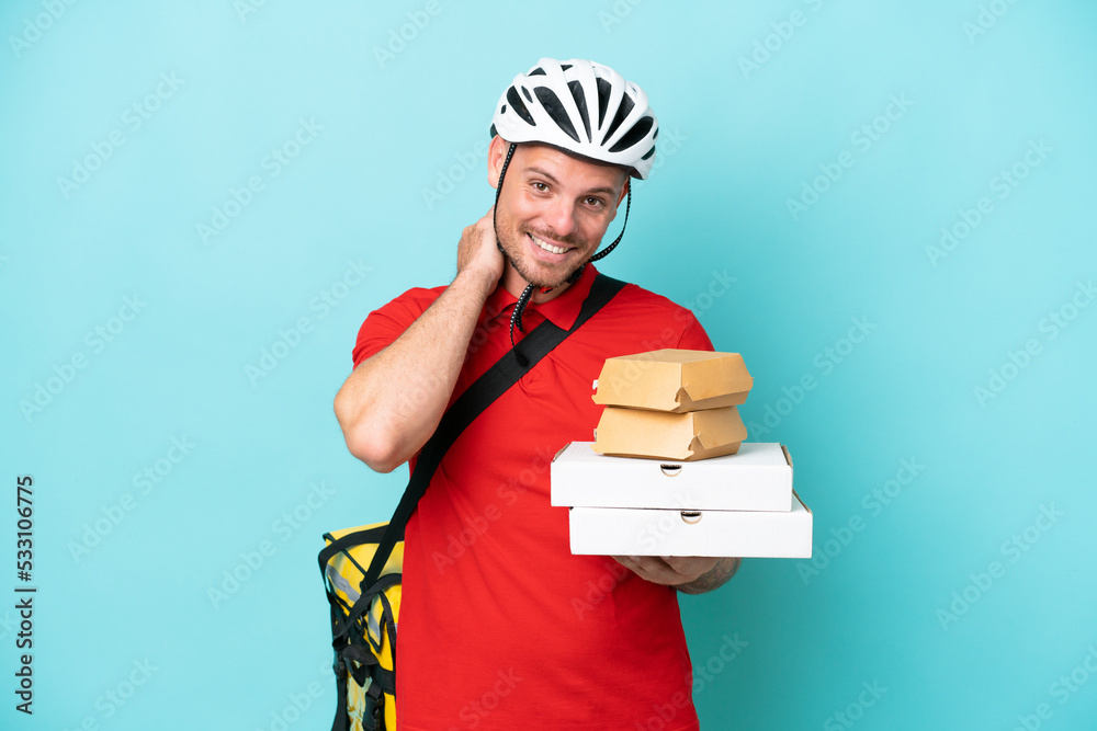 Young caucasian man with thermal backpack and holding fast food isolated on blue background laughing Young caucasian man with thermal backpack and holding fast food isolated on blue background laughing