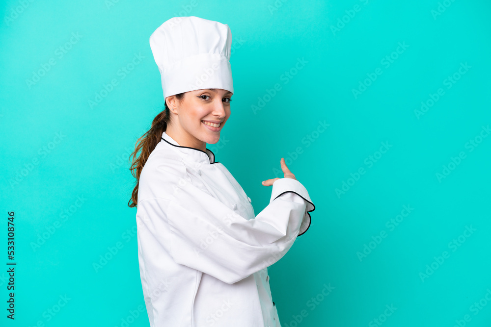 Young caucasian chef woman isolated on blue background pointing back