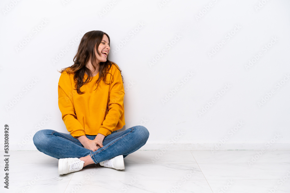 Young caucasian woman sitting on the floor isolated on white wall laughing in lateral position Young caucasian woman sitting on the floor isolated on white wall laughing in lateral position