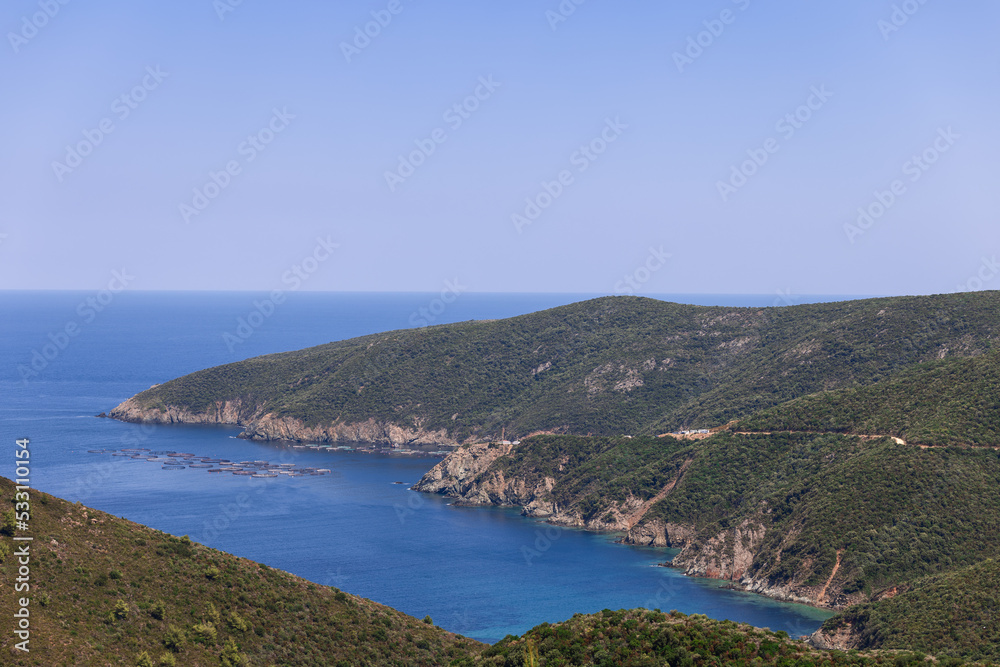 Mussel farm in blue water Aegean sea next to historic Greek territory covered with green stunted vegetation of southwest edge of Sithonia peninsula in Toroni municipality, Chalkidiki, Greece.