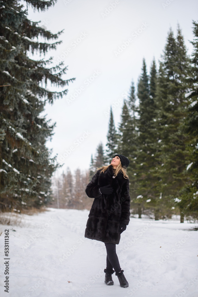 irl in a black hat and a fur coat stands on a snowy winter alley