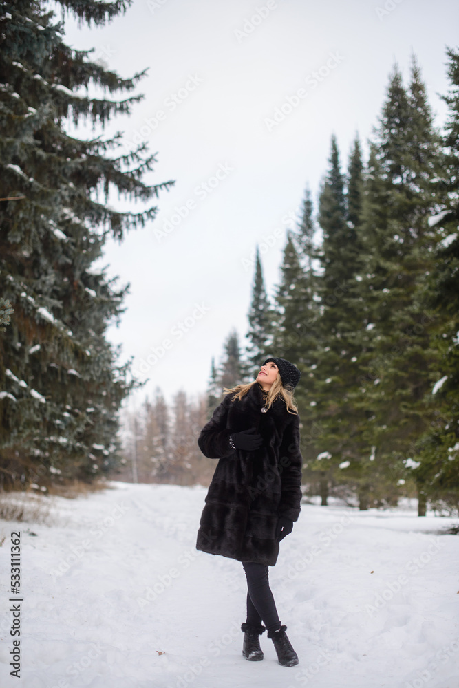 irl in a black hat and a fur coat stands on a snowy winter alley irl in a black hat and a fur coat stands on a snowy winter alley