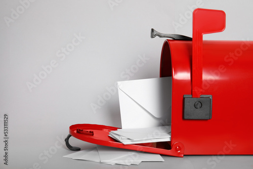 Open red letter box with envelopes on light background, closeup. Space for text