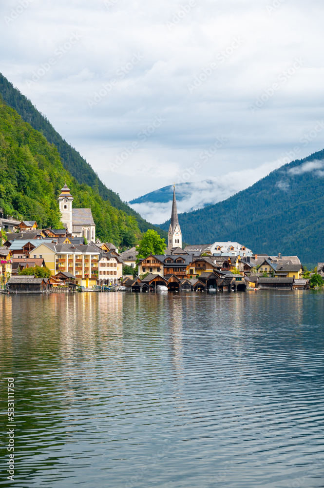Hallstatt Village and Hallstatter See lake in Austria. Scenery with famous old church near the lake. Clouds and mist over the mountains in background. Famous tourist destination.