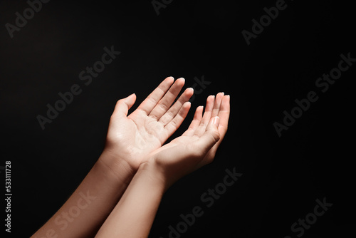 Woman stretching hands towards light in darkness, closeup