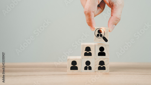 Hand hold wood cubes with magnifying glass focuses on the best employee icon to be a team leader for recruitment managers, and target customer concepts. HRM or Human Resource Management.
